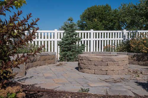 A fire pit is sitting on a patio next to a white fence.