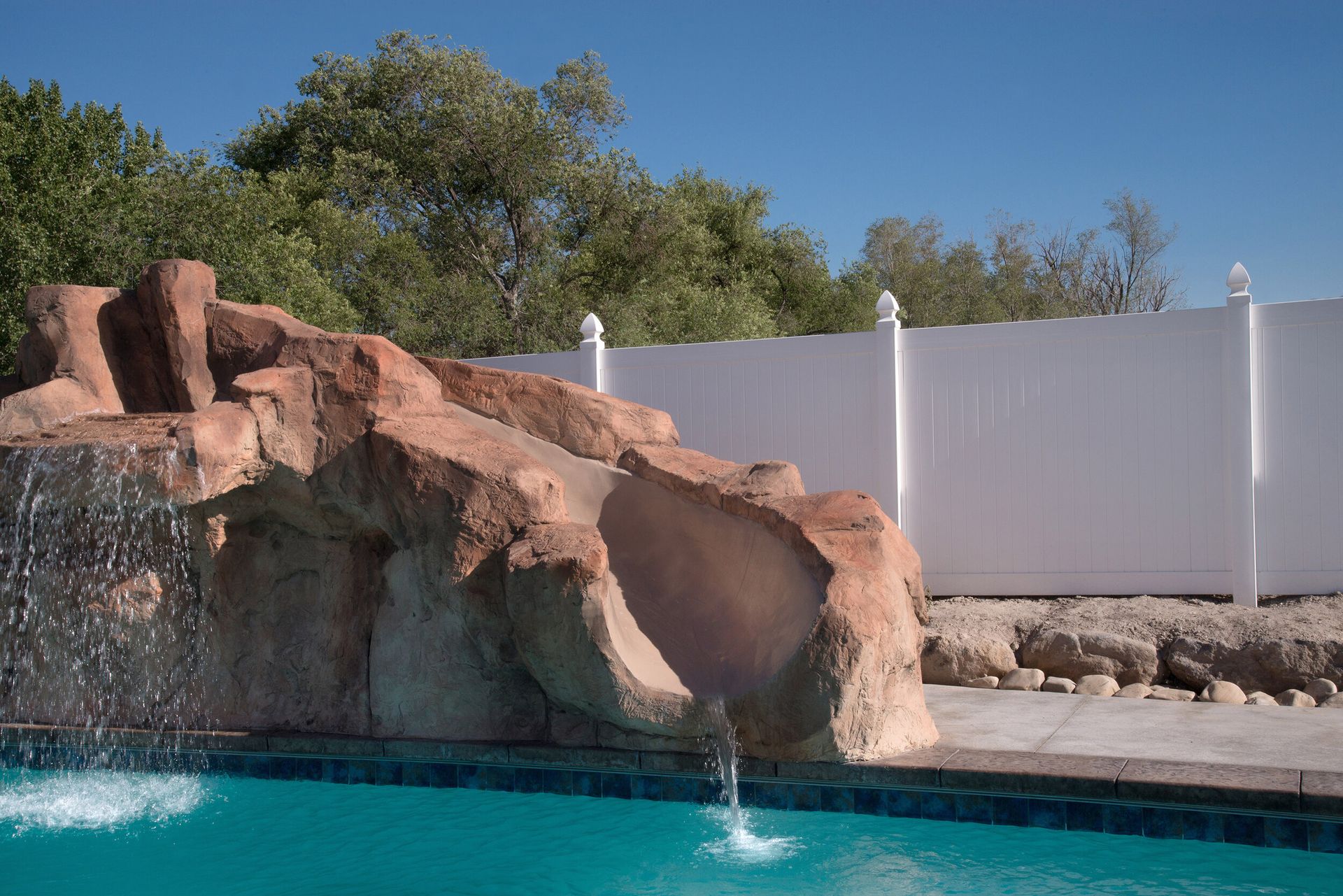 A swimming pool with a waterfall and a white fence