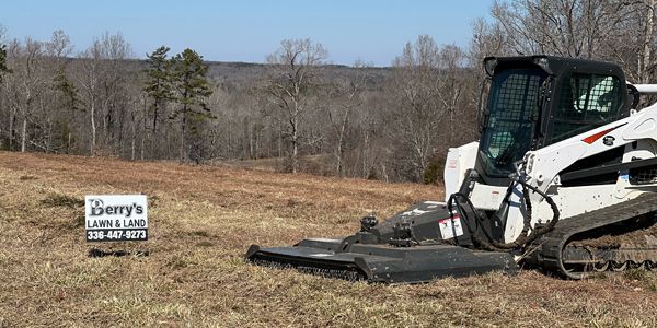 A bulldozer is cutting grass in a field next to a sign.