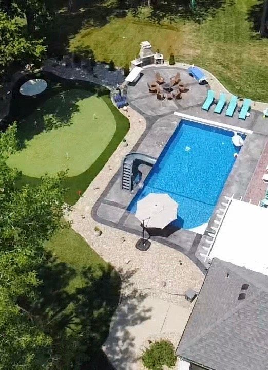 Aerial view of a backyard with a pool, putting green, fire pit, and lounge chairs.