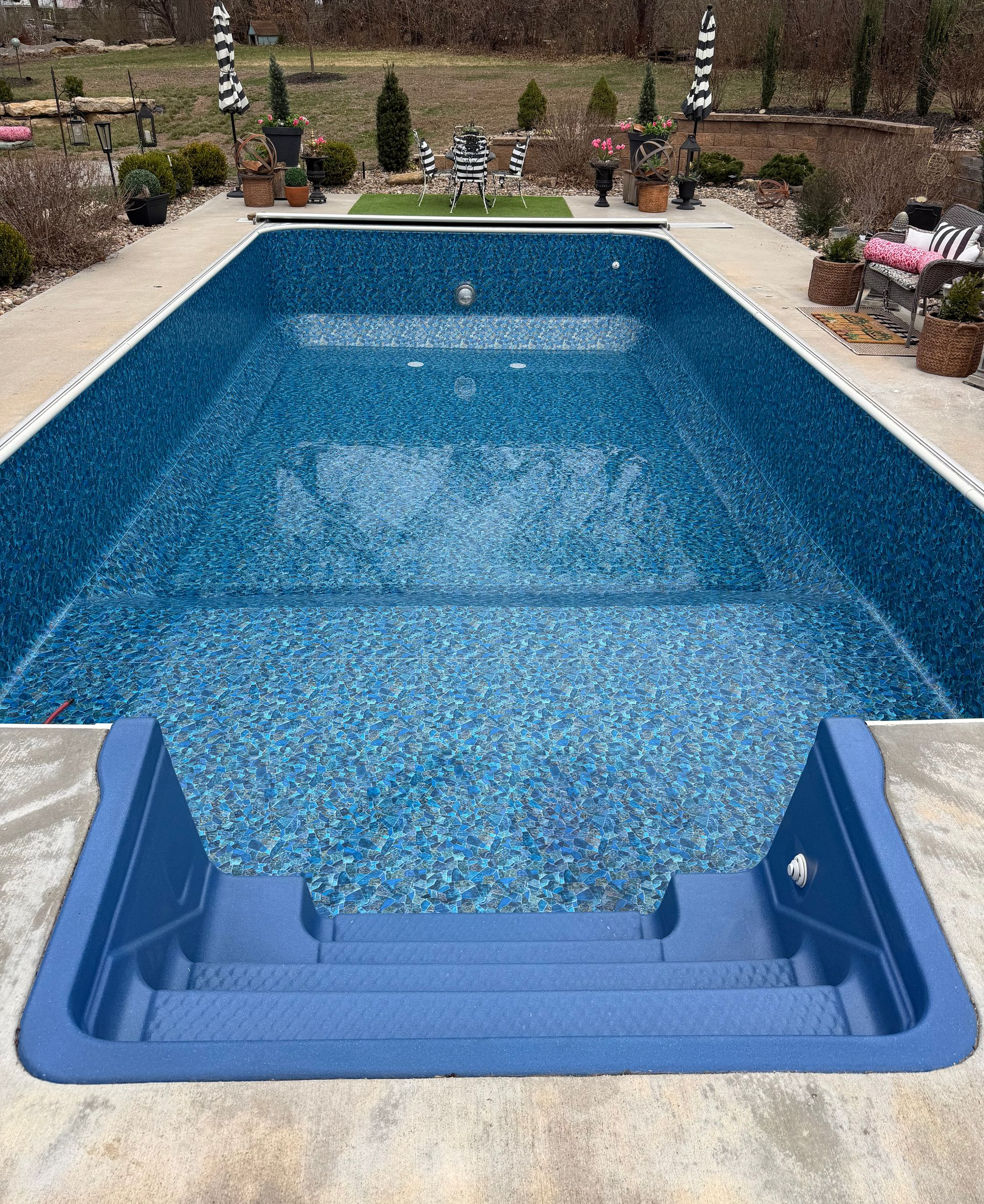 A rectangular backyard swimming pool with a blue patterned liner and blue integrated stairs at the shallow end. 