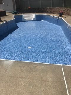 Empty blue-tiled swimming pool with concrete edges and steps. Sunny outdoor setting.