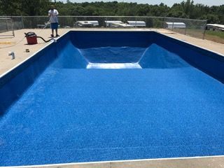 Blue-lined empty swimming pool. A person is vacuuming the pool deck.