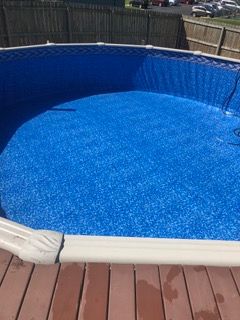 An empty above-ground pool with a blue speckled interior, surrounded by a wooden deck and a fence.
