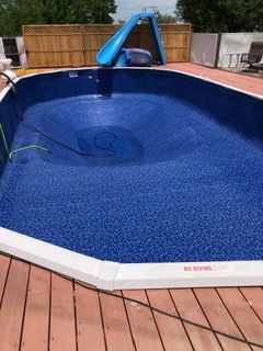 Empty blue-lined swimming pool with slide on a wooden deck.