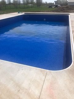 A rectangular swimming pool filled with blue water, set in a concrete patio.