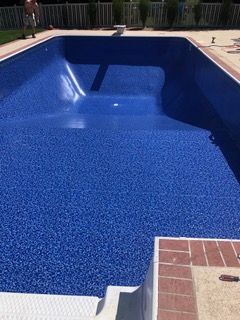 Empty blue tiled swimming pool, with a brick border and stairs.