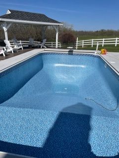 Empty blue swimming pool with white gazebo and fence in background, clear blue sky.
