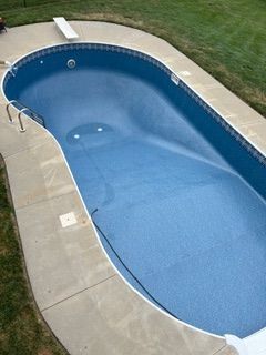Empty blue swimming pool with concrete surround and diving board, outdoors.