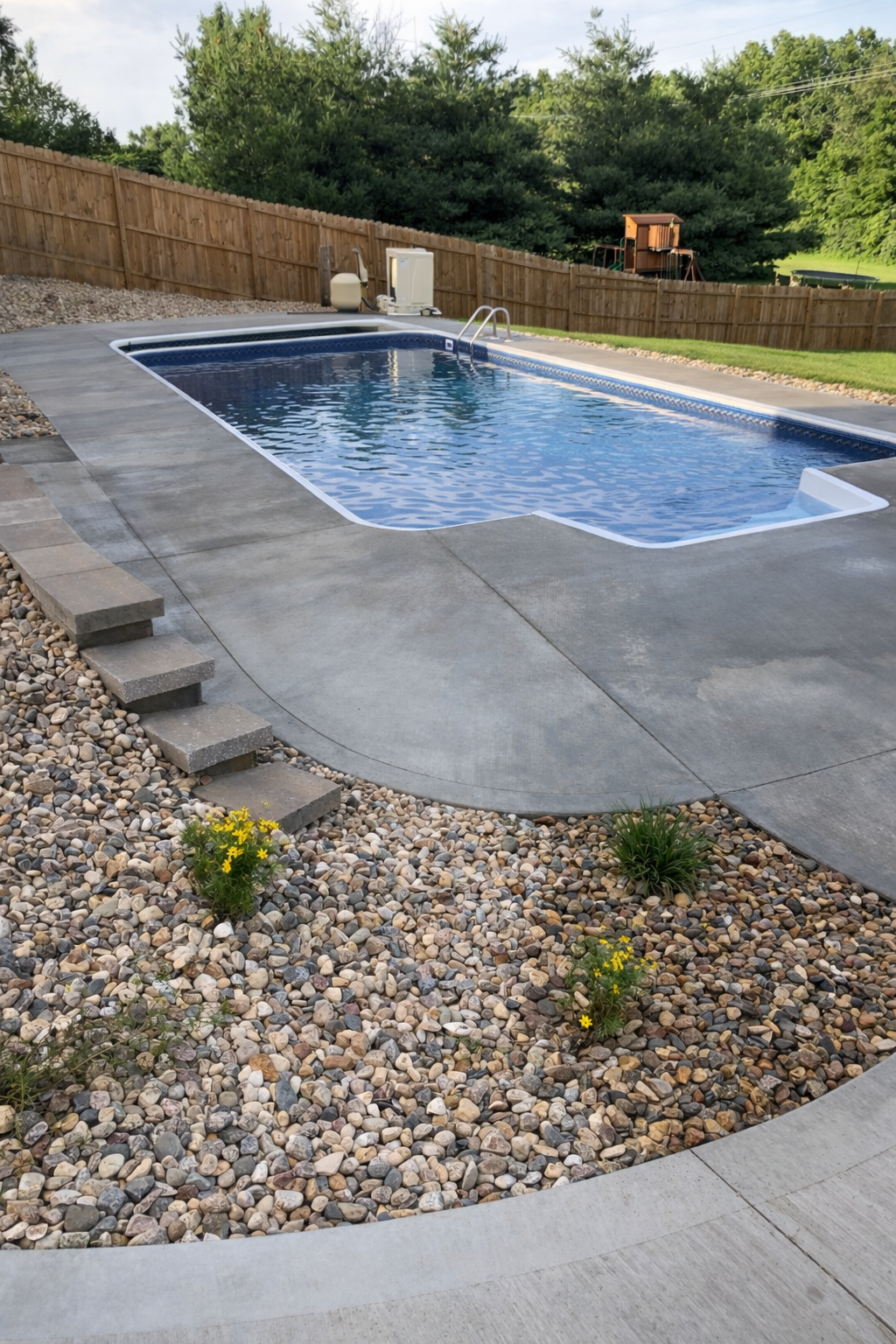 Rectangular pool surrounded by concrete and landscaping, with a rock garden and steps.