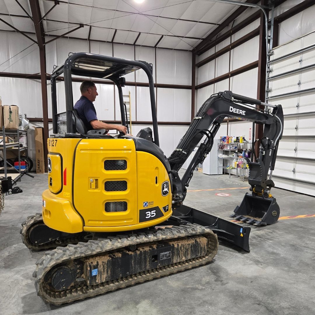 Two men digging with shovels near orange cones and an excavator, outside on a sunny day.