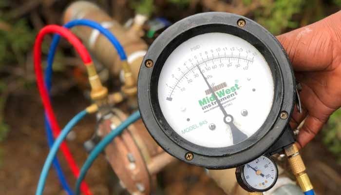 Close-up of a pressure gauge attached to pipes with red and blue hoses. The needle points to 45.