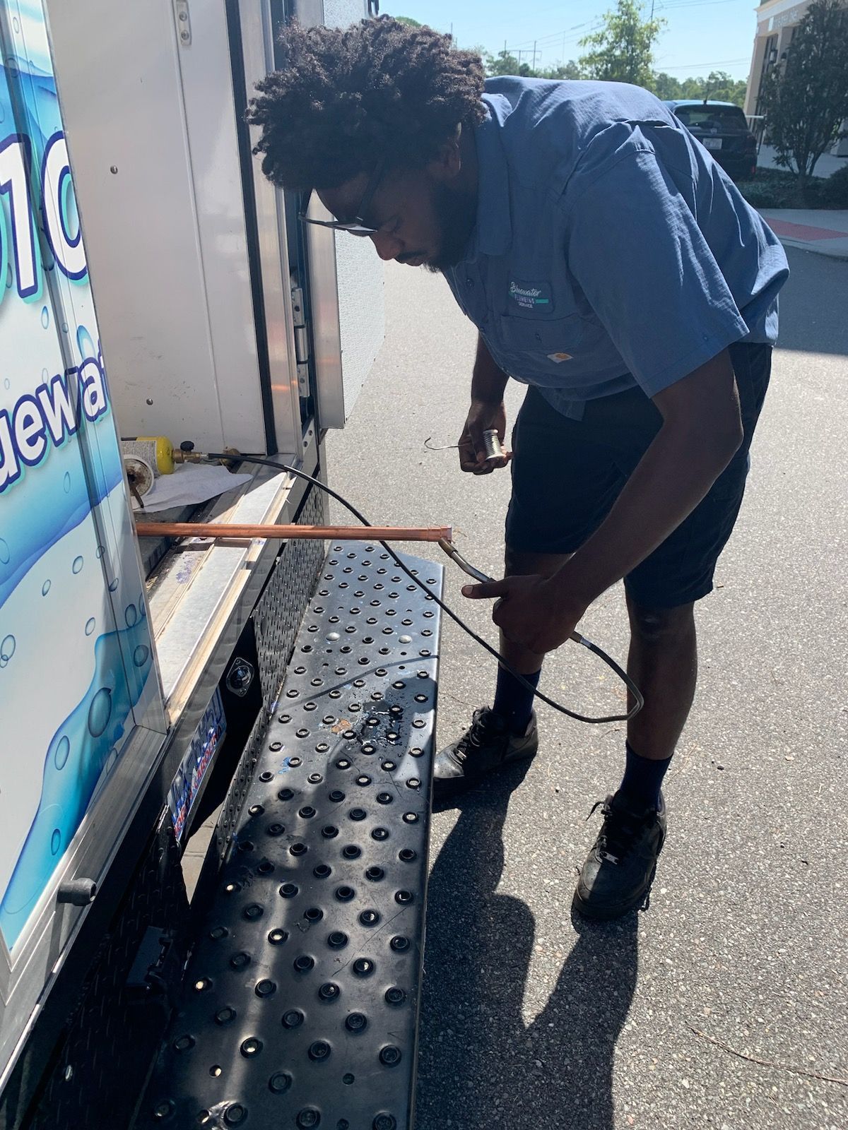 Man in blue shirt working on the back of a water delivery truck on a sunny day.