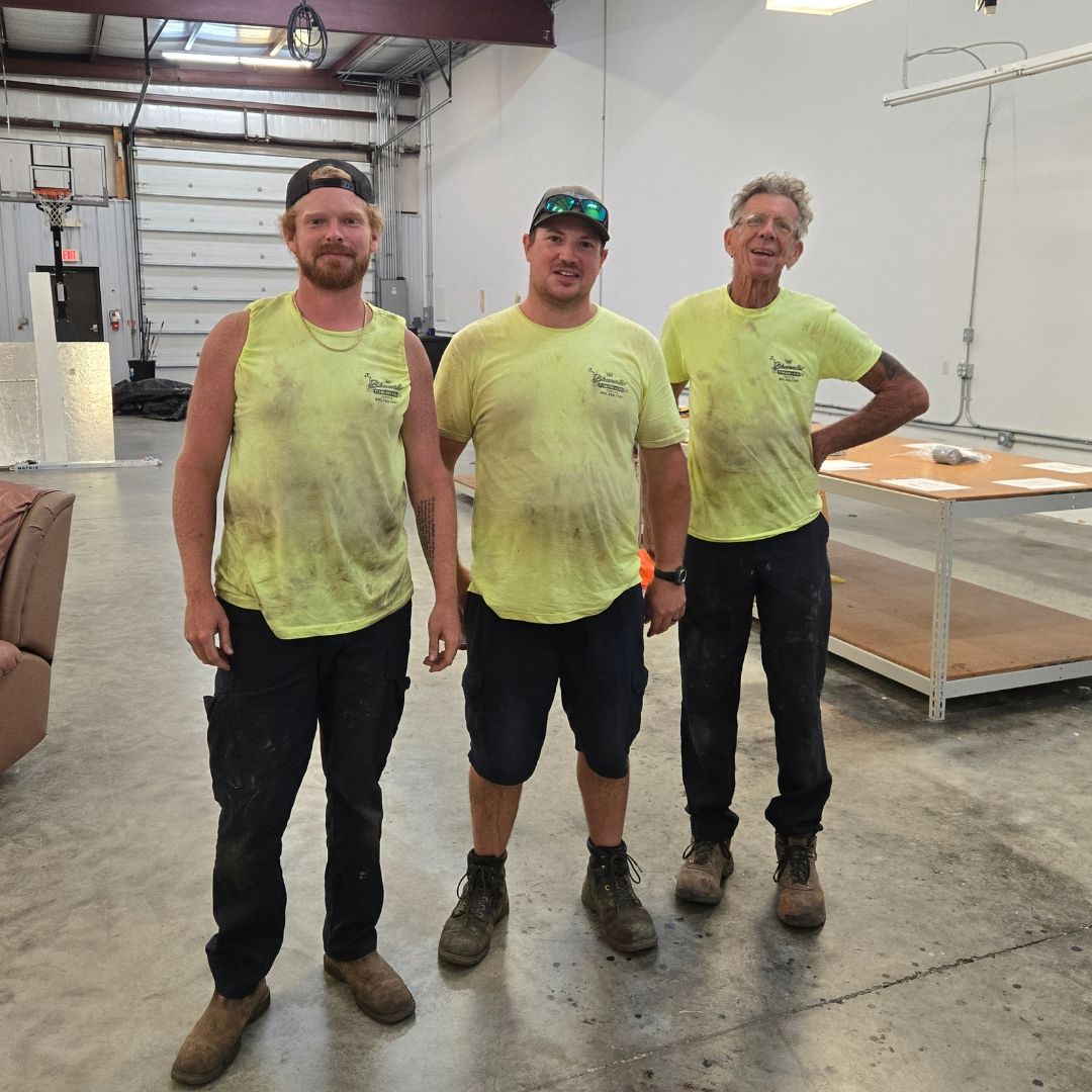 Three men in yellow shirts and work clothes stand inside a warehouse.