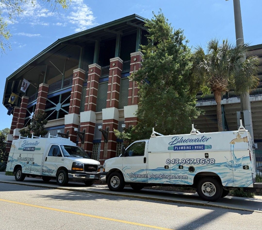 Two Clearwater Plumbing trucks parked in front of a brick building.
