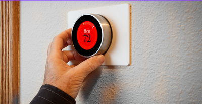 Hand turning a smart thermostat dial, setting it to 72 degrees.
