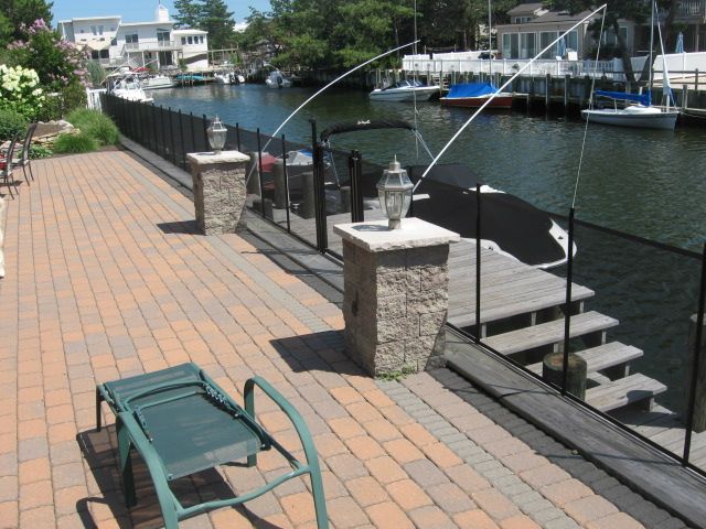 Brick waterfront walkway with black fence, green chair, lanterns, and boats on the water