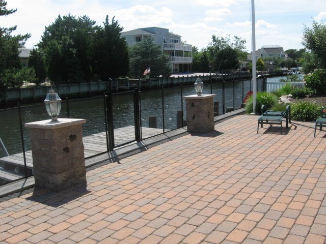 Riverside brick patio with benches, stone posts, and a black fence along the water