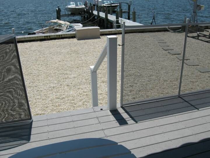 White deck gate opening to a waterfront dock with blue water and boats in the background