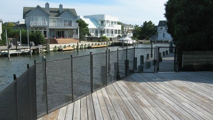 Wooden boardwalk beside a canal with waterfront houses and a chain-link fence
