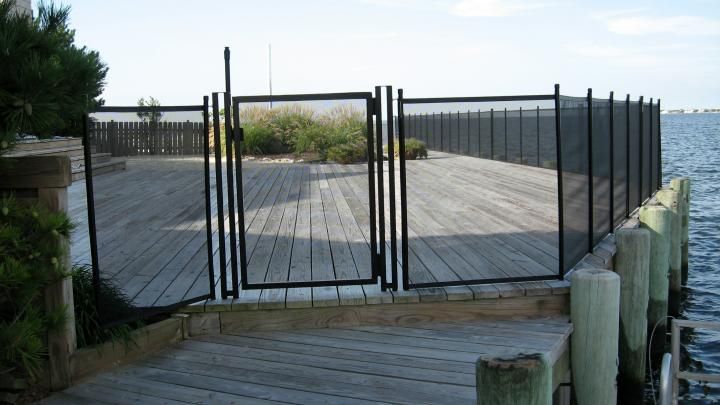 Wooden boardwalk leading to a gated seaside deck with ocean view and posts along the edge