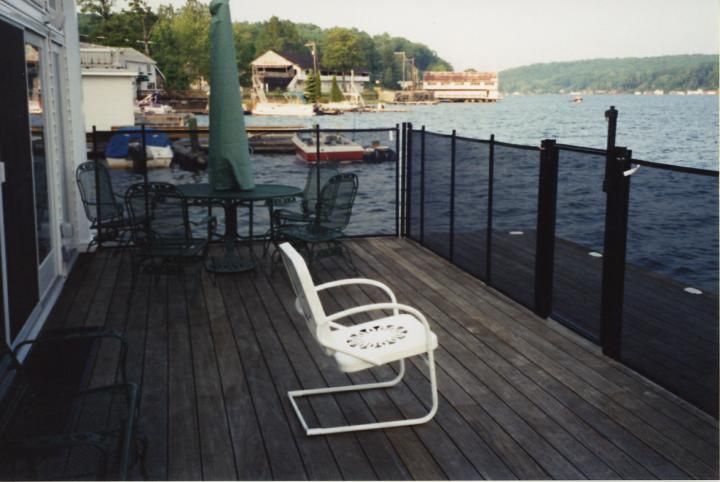 Wooden lakeside deck with white chair, tables, and black railing beside the water