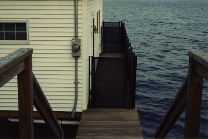 Wooden stairs beside a house lead down to a dock over dark, choppy water.