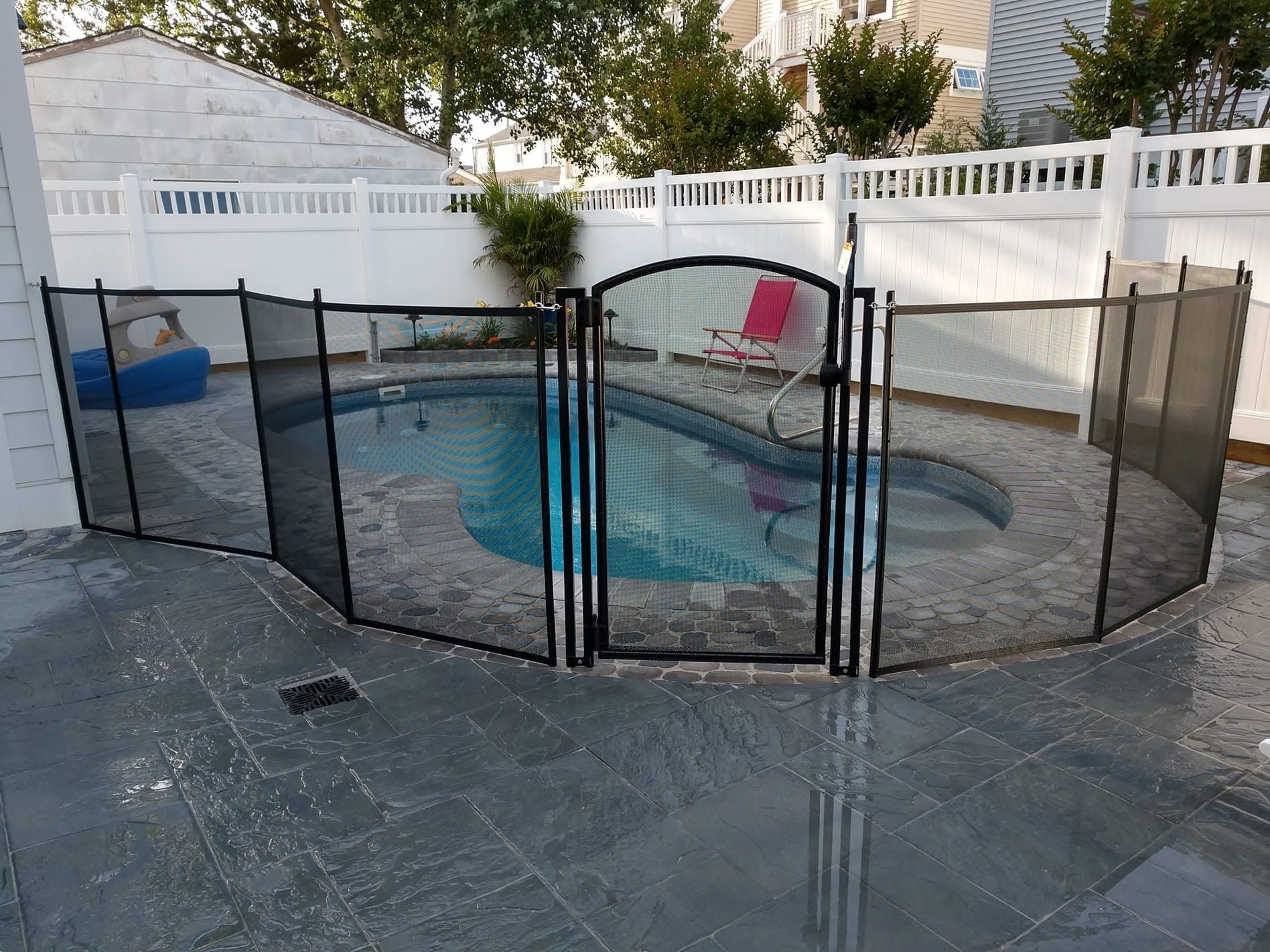 Backyard swimming pool surrounded by a black safety fence and a covered pool chair.