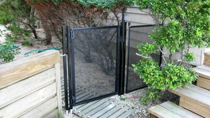 Black mesh gate in a wooden fence beside a garden path and greenery