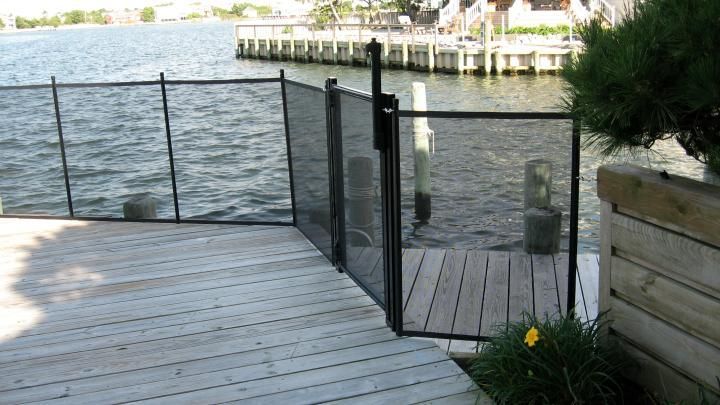 Wooden deck with black railing and gate beside a waterfront dock and calm water