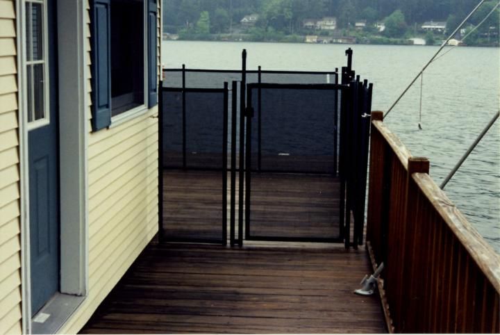 Wooden deck beside a lake, with a black gate and yellow house siding on the left.