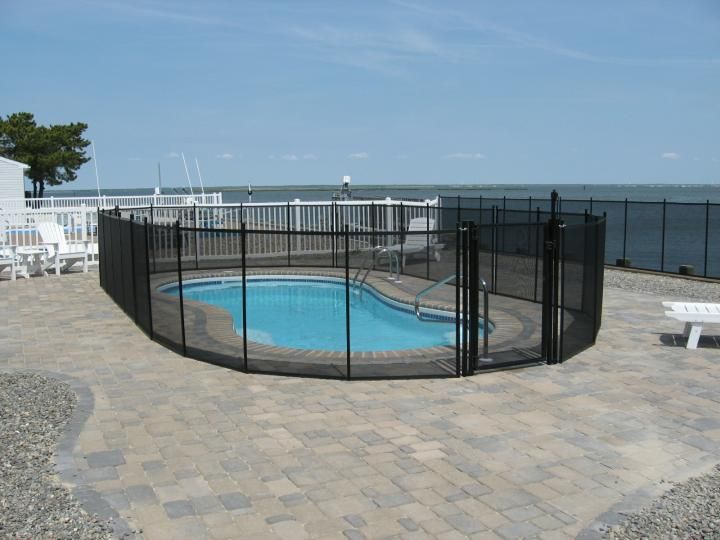Fenced-in outdoor pool beside a paved patio and ocean view