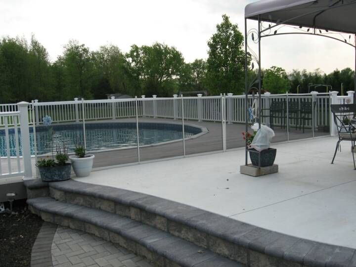 Outdoor pool deck with white railing, curved stone steps, potted plants, and trees in the background