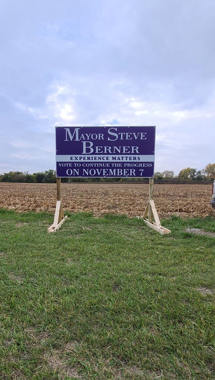 A large sign is sitting in the middle of a grassy field.