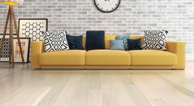 Yellow sofa with patterned pillows in front of a brick wall and light wood floor.