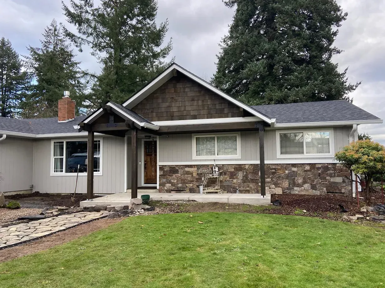 Gray and brown house with stone facade, dark brown accent roof, and green lawn.