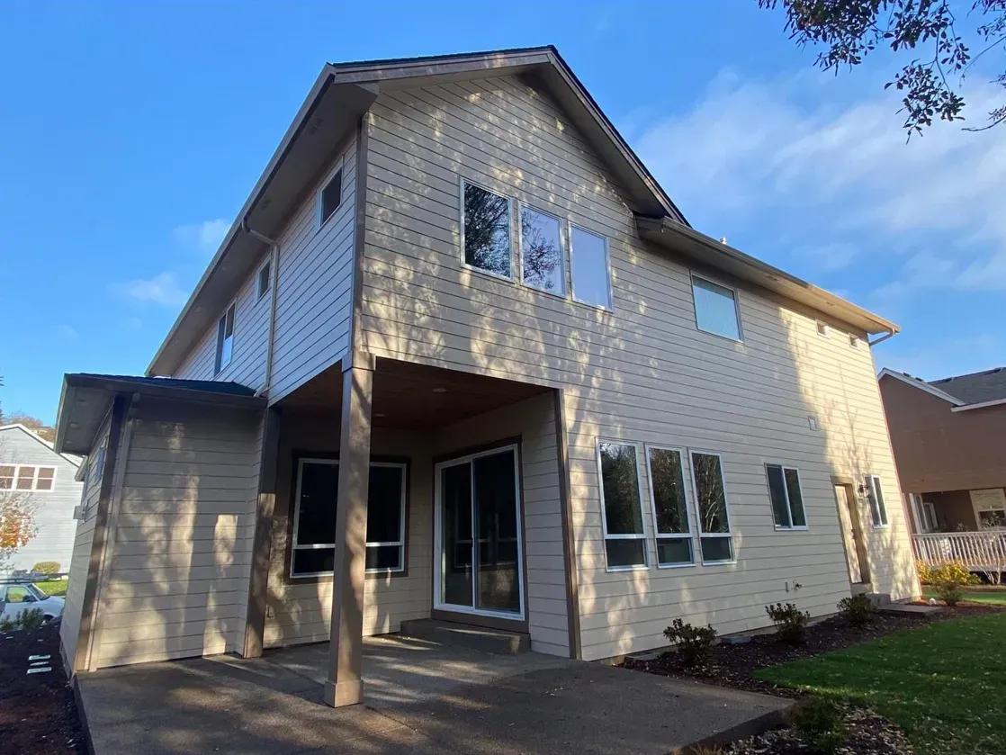 Two-story beige house with a covered patio, large windows, and a blue sky background.
