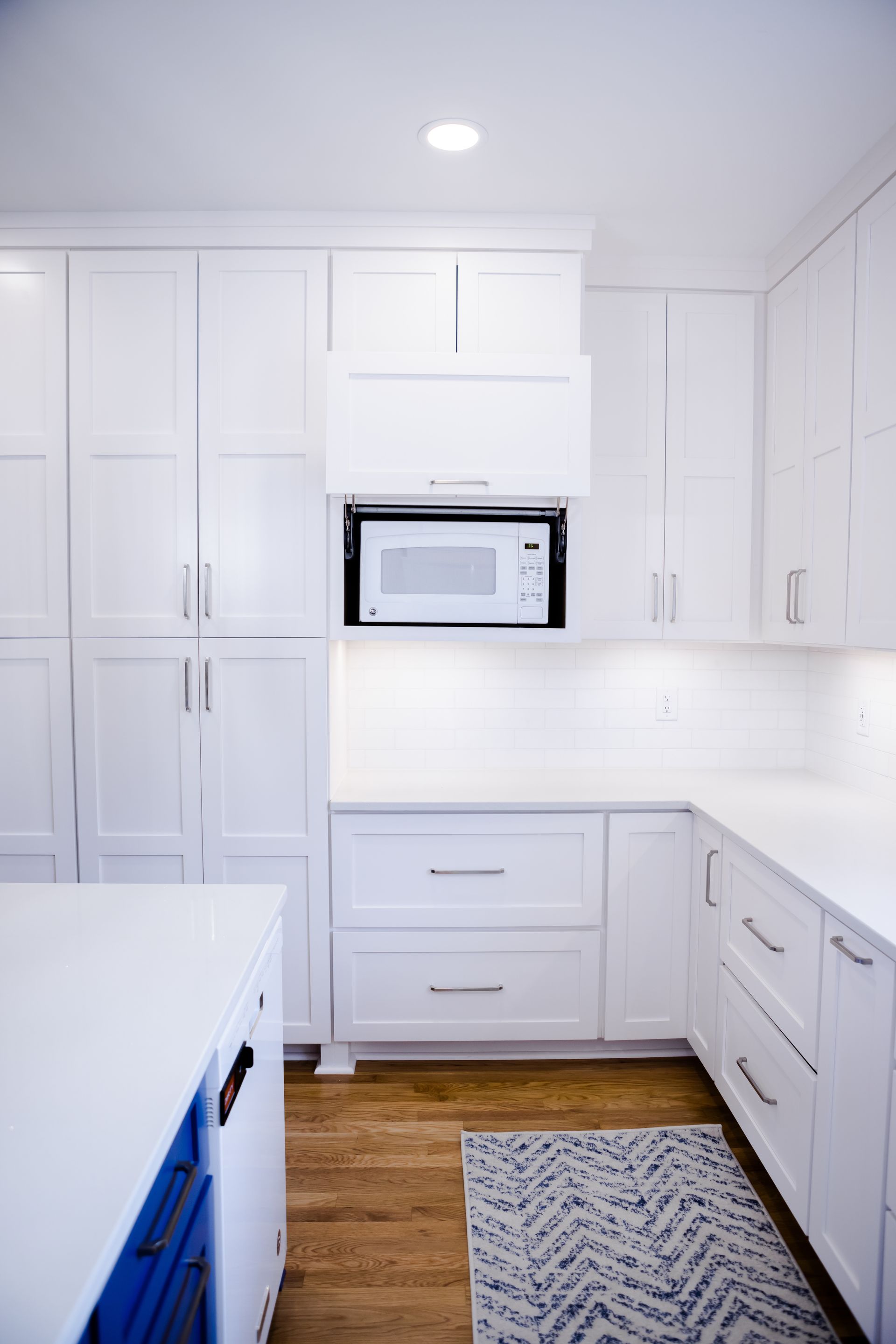 White kitchen with built-in microwave, cabinets, drawers, and a blue-accented island on wood flooring.