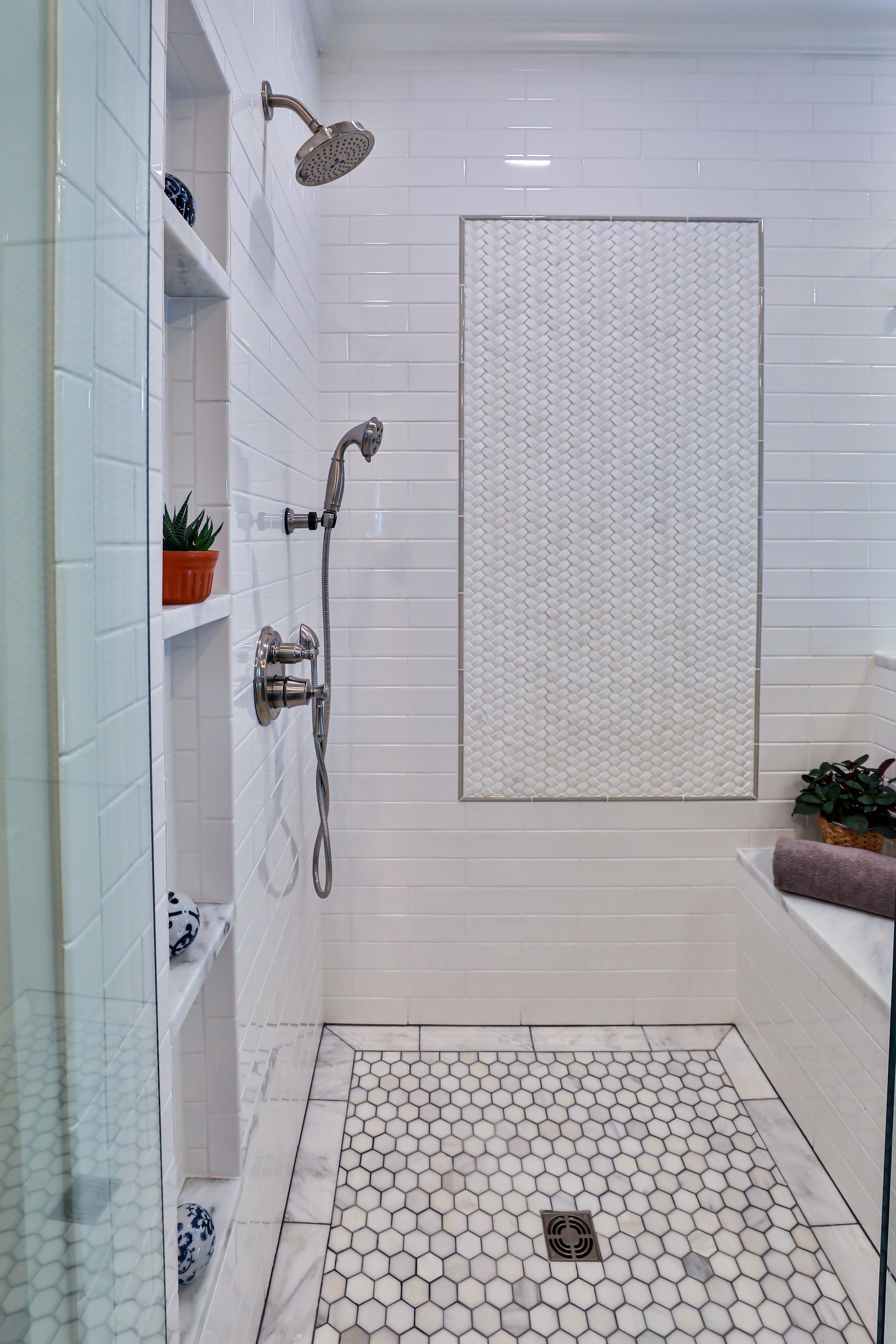 White tiled shower with built-in shelves, a handheld shower, and a mosaic tile floor.