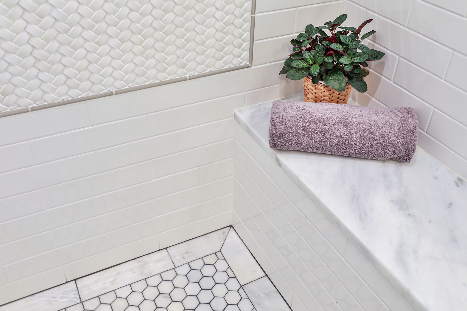 White-tiled shower with a marble bench holding a rolled towel and a potted plant. Hexagon floor tiles.