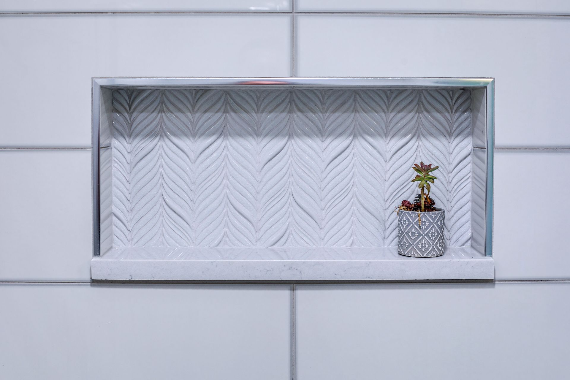 Recessed bathroom shelf with white patterned tiles, holding a small succulent in a decorative pot.