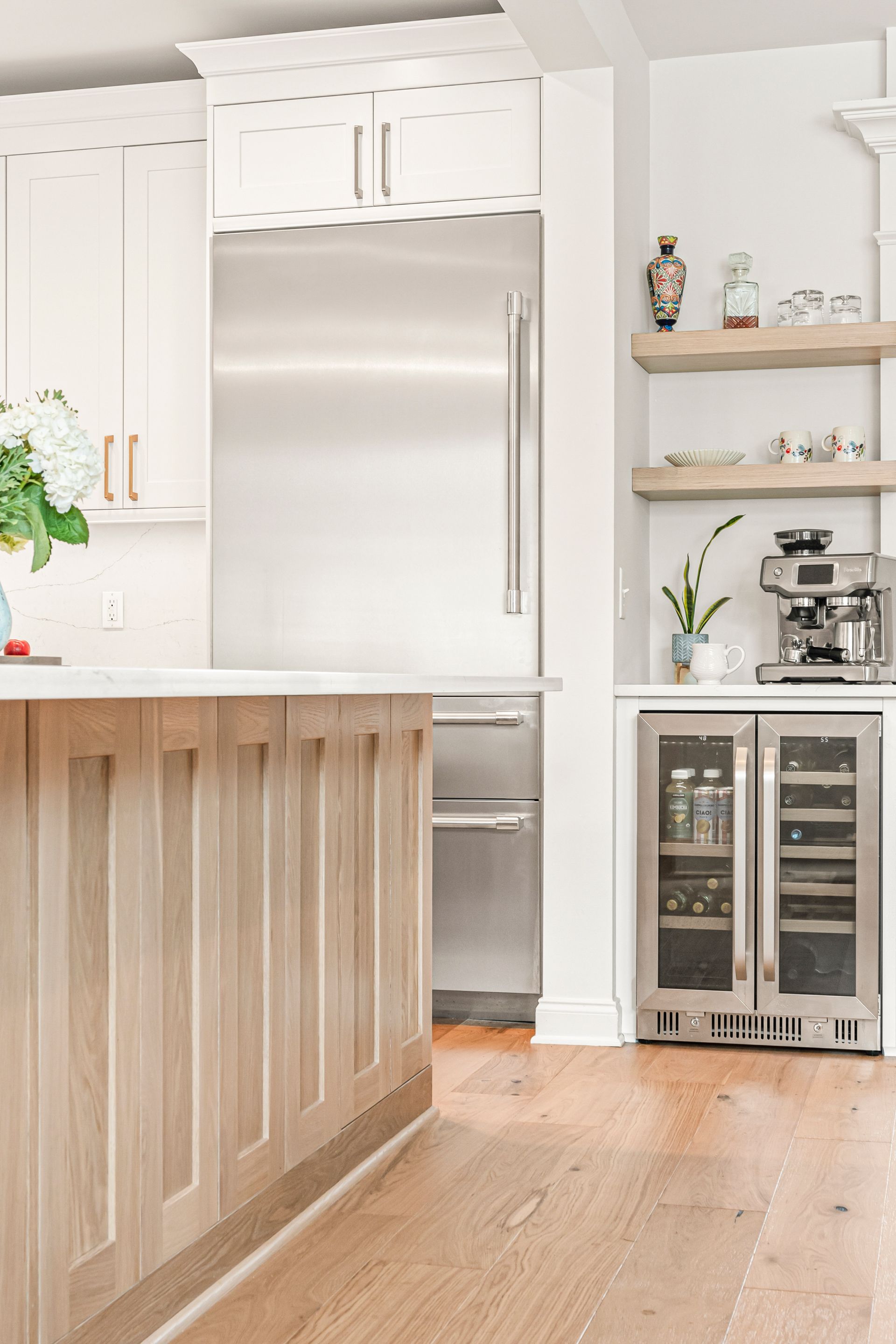 Kitchen with light wood island, stainless steel appliances, white cabinets, and open shelving.