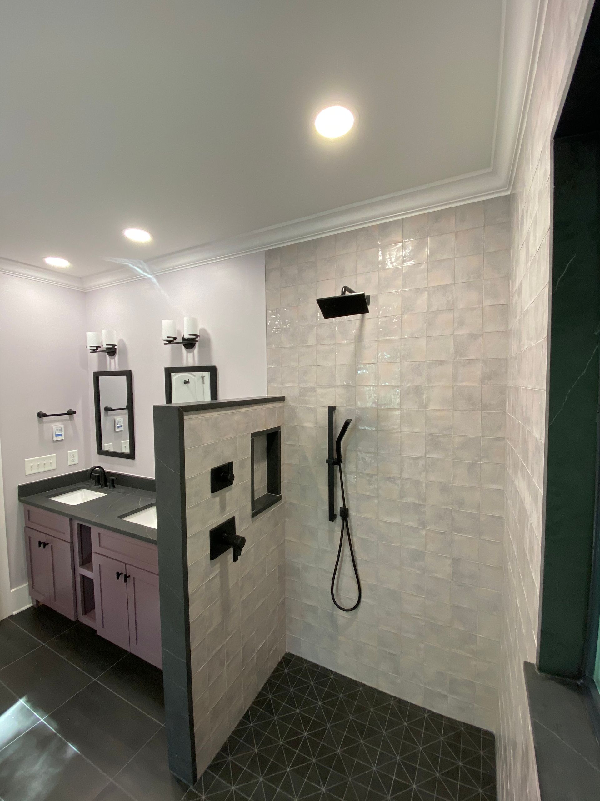Modern bathroom with purple vanity, walk-in shower with black fixtures and gray tile, and a dark floor.