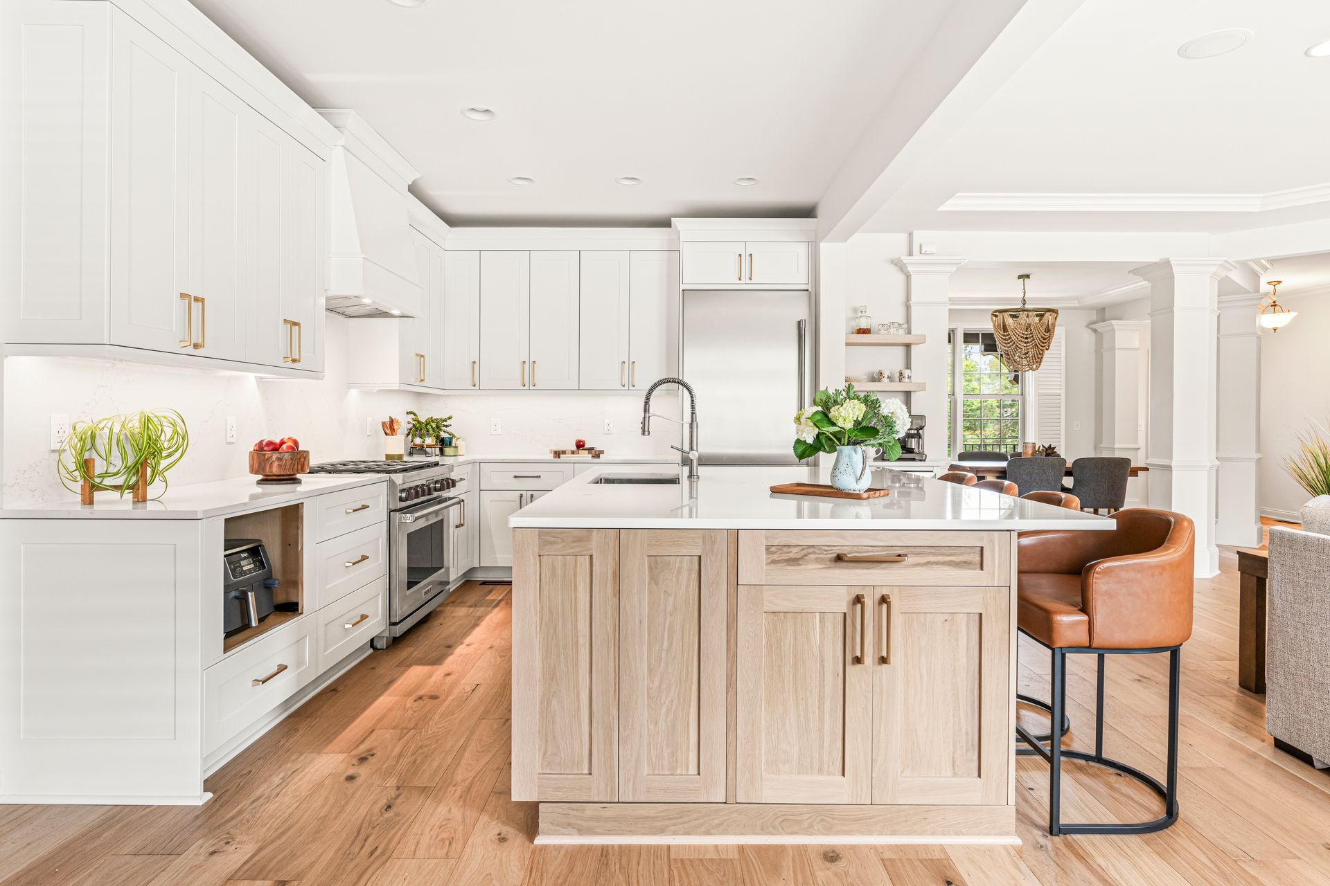 Bright white kitchen with wood floors and light-colored island, and tan leather barstool.