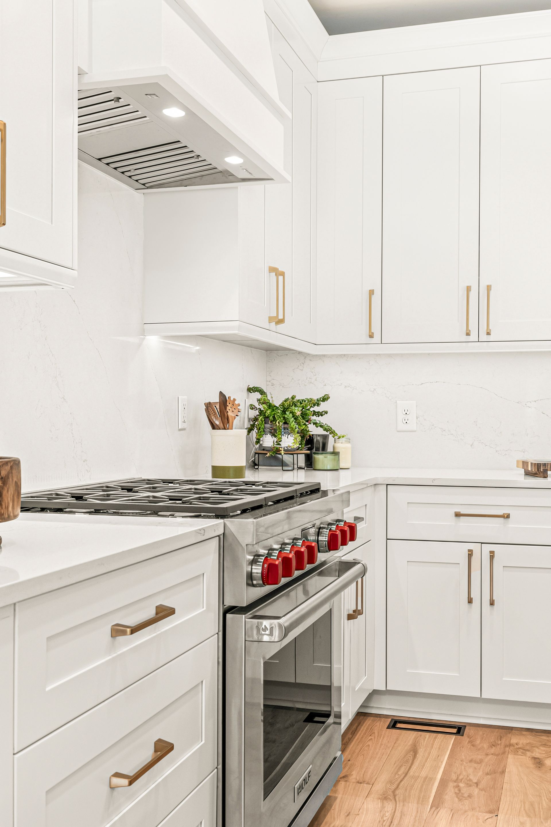 White kitchen with stainless steel appliances, gold hardware, and wood floors.