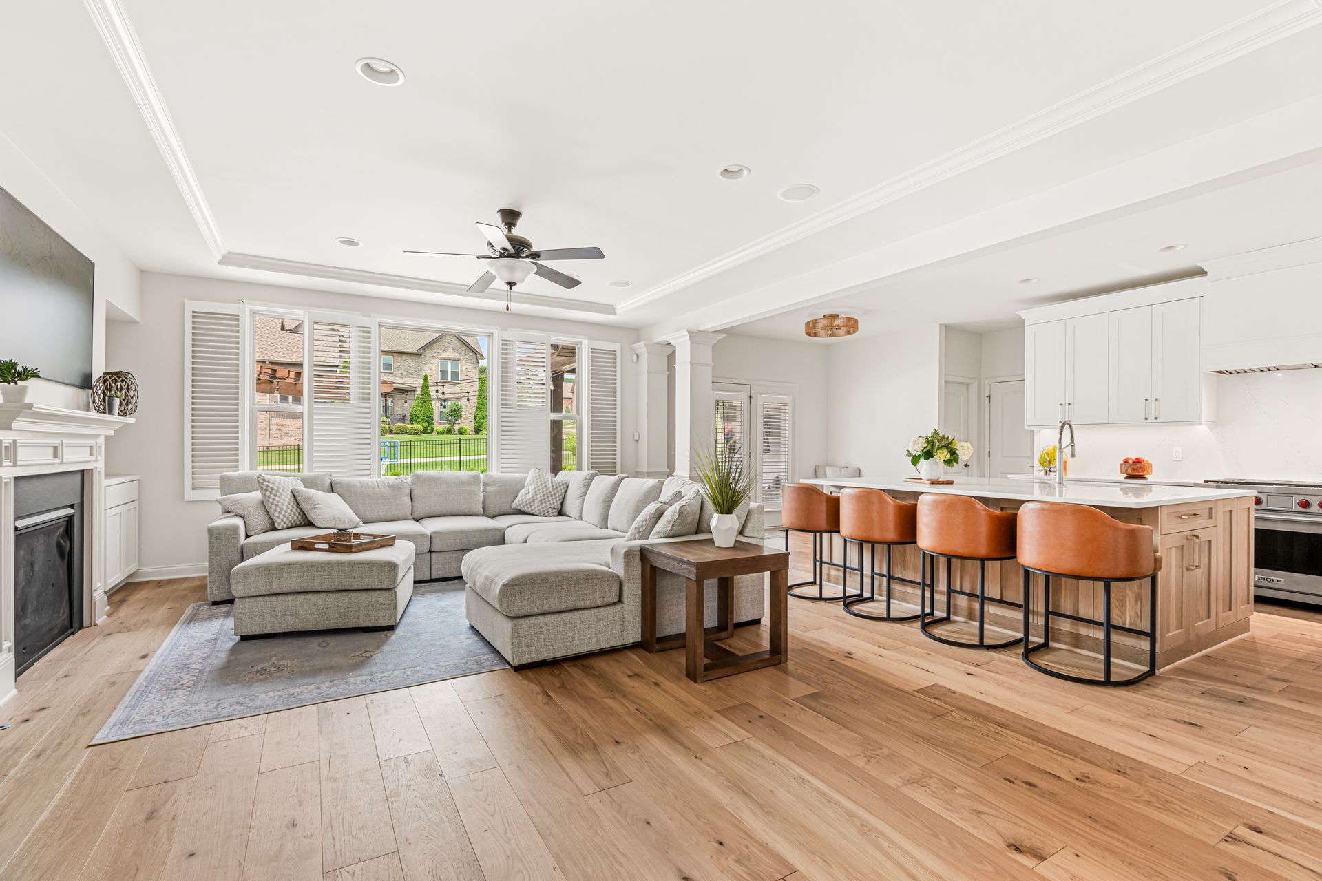 Spacious open-concept living area with hardwood floors, large sectional, kitchen island with bar stools, and windows.