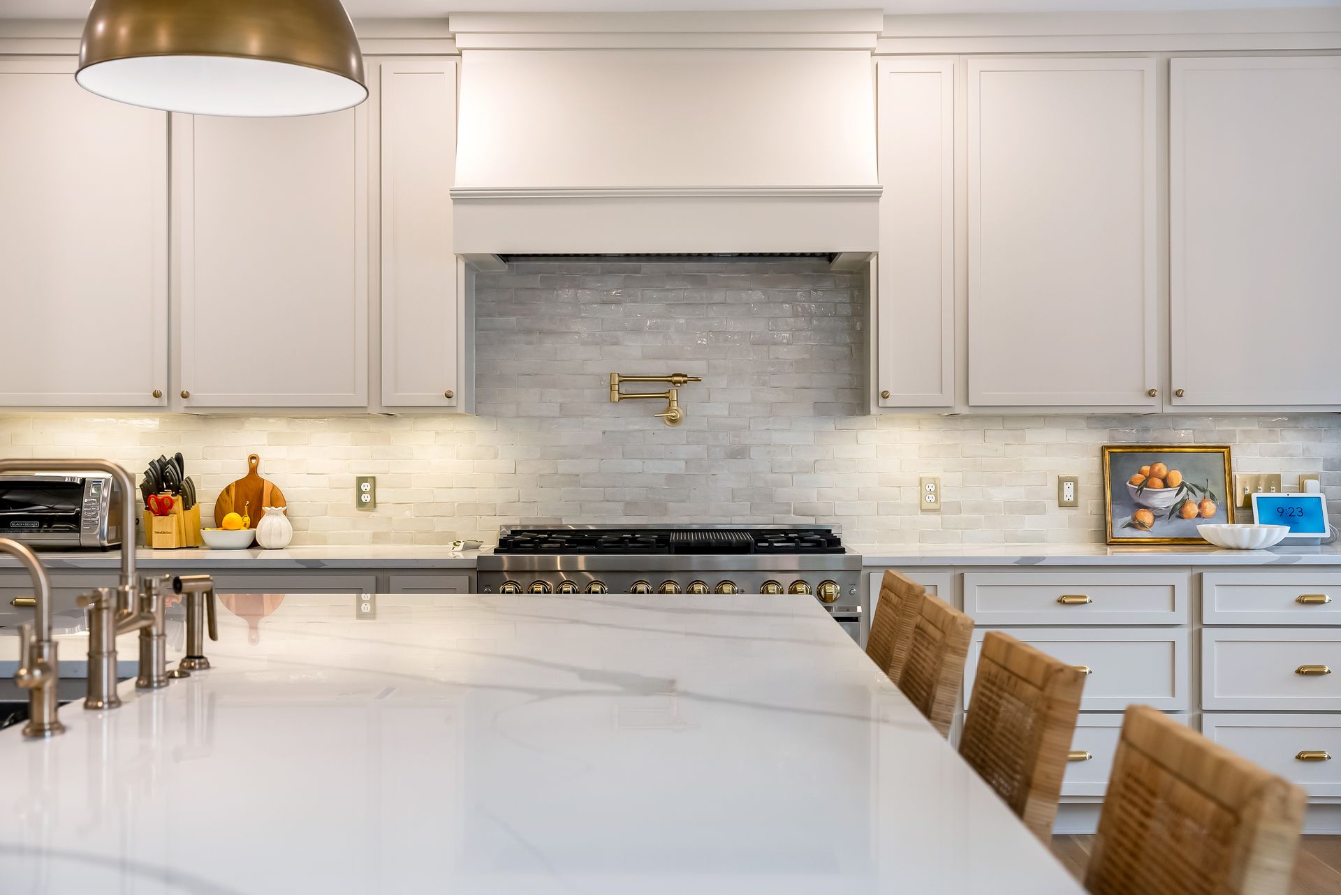Kitchen with white cabinets, marble countertops, stainless steel appliances, and woven bar stools.
