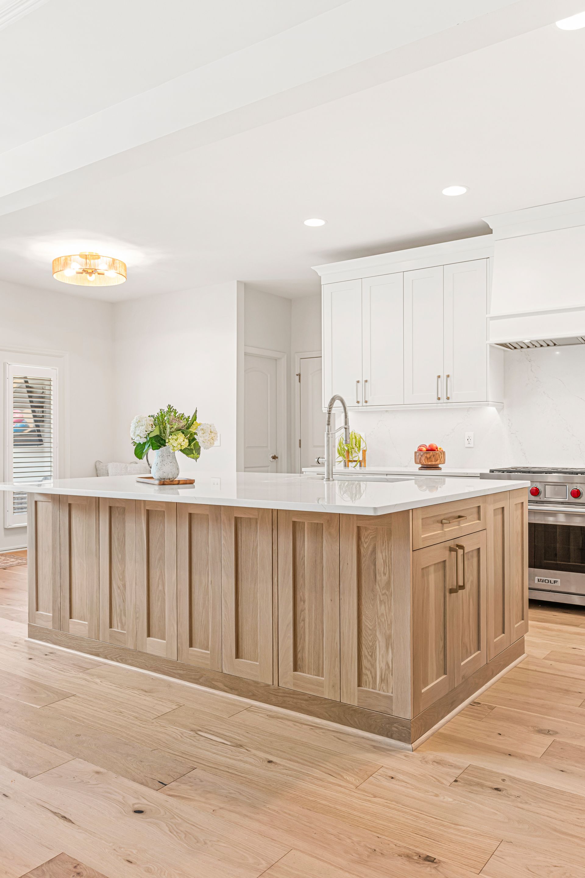 Spacious kitchen with light wood cabinets and island, white countertops and walls.