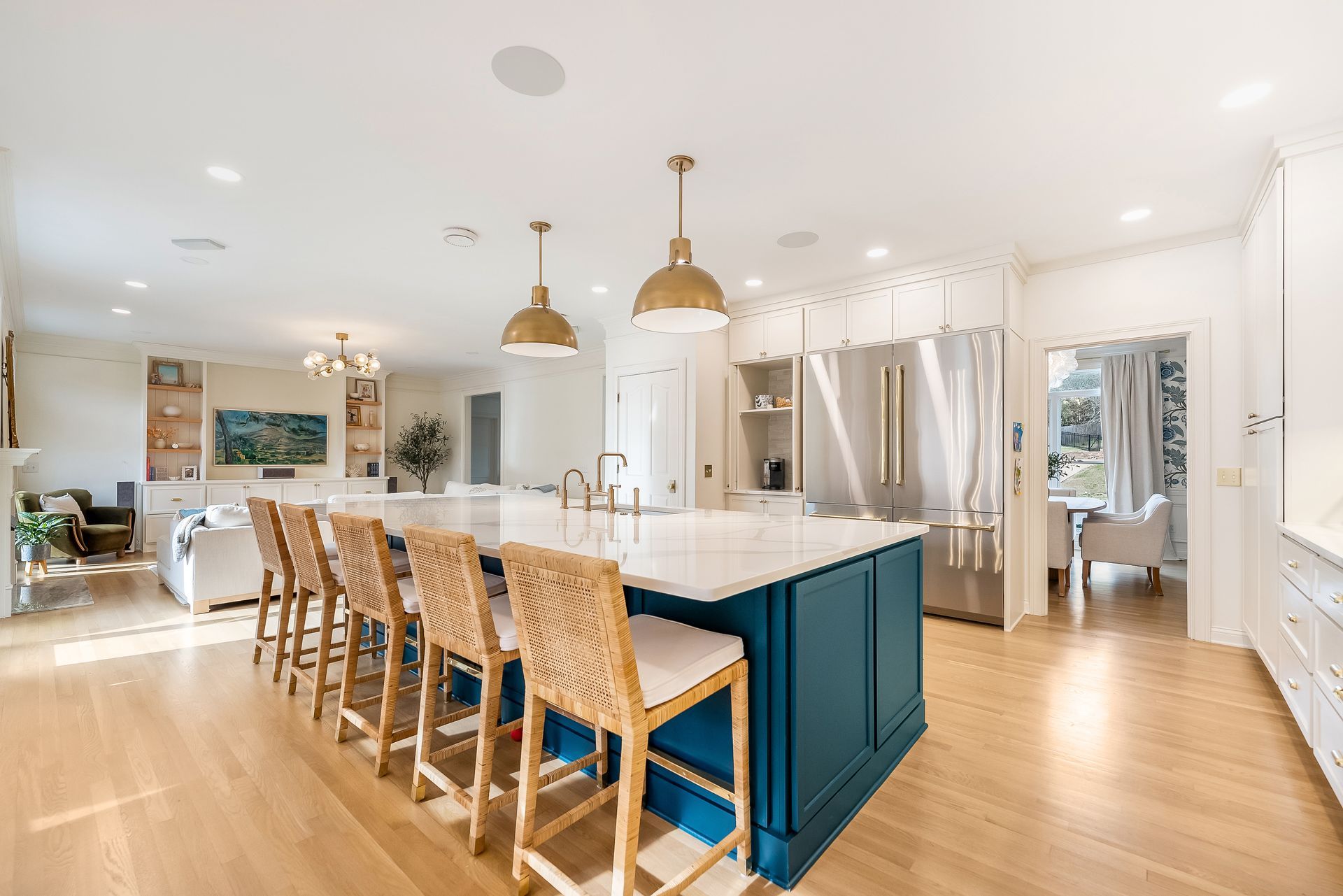 Spacious kitchen with blue island, gold pendant lights, wood floors, and woven bar stools.