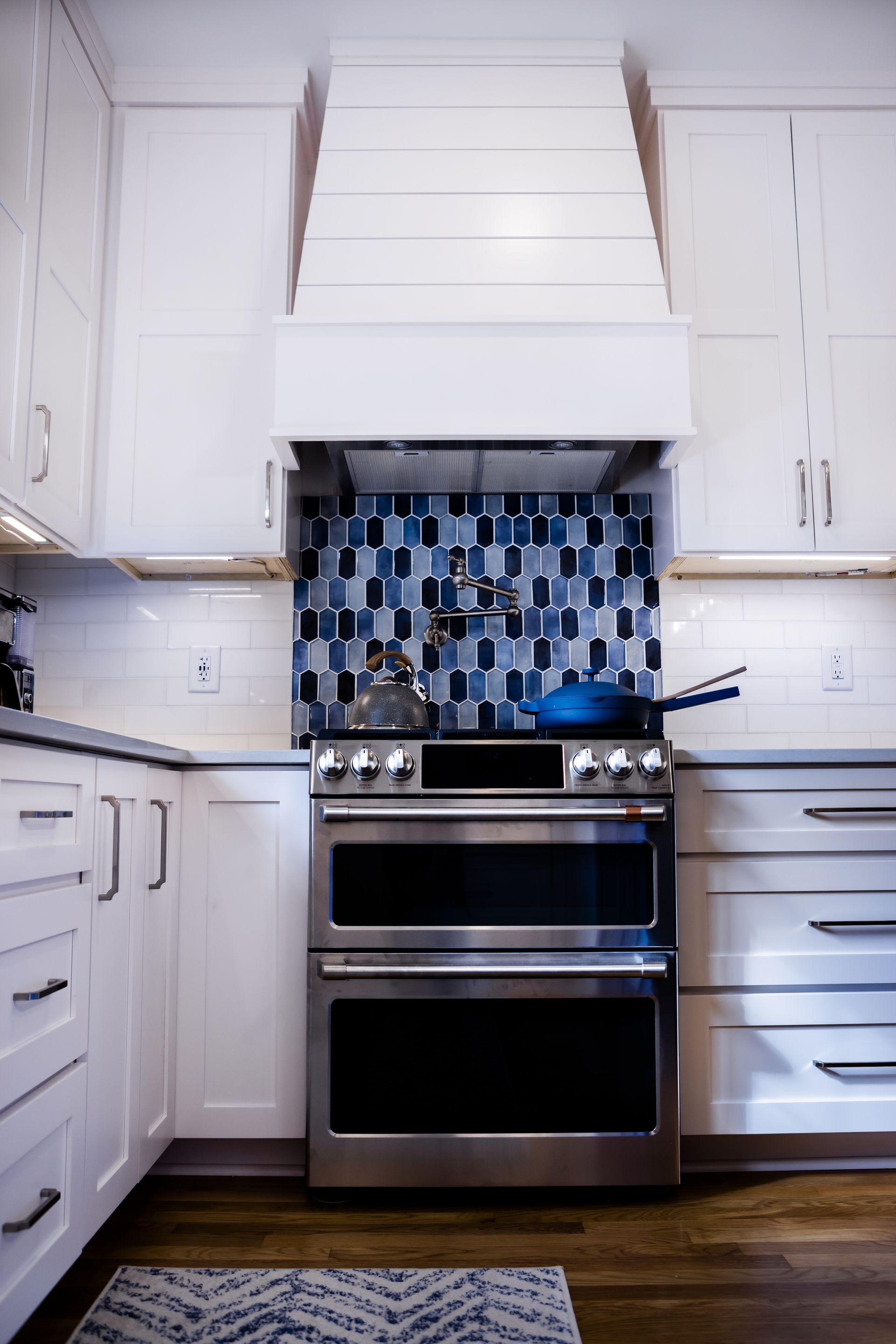 White kitchen with stainless steel stove, blue backsplash, and wooden floor.